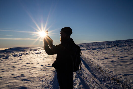 man trekking at taking pictures in winter sunset