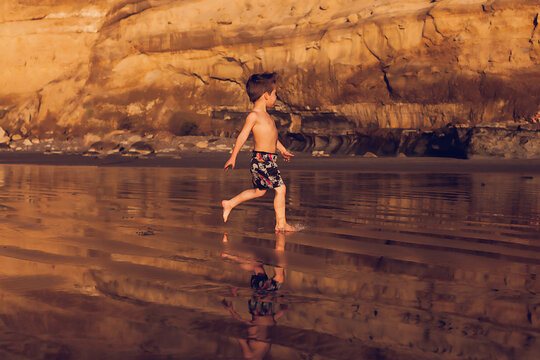 Little boy running at the beach at low tide with cliffs on background.