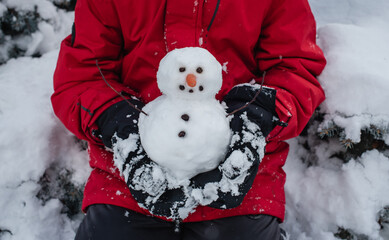 Child holding a small snowman in his hands outdoors on a snowy day.