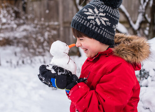 Boy holding a small snowman in his hands outdoors on a snowy day.