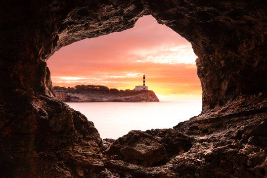 Portocolom lighthouse at sunrise from natural stone cave in Majorca