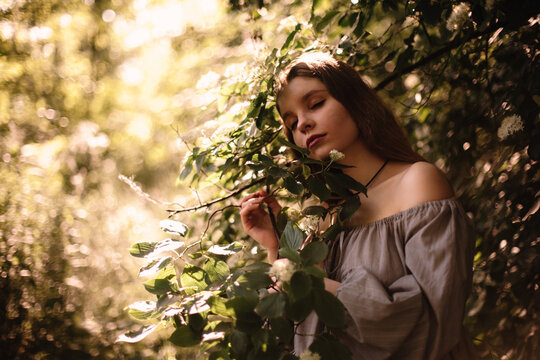 Peaceful young woman standing by flowering branches in park in summer