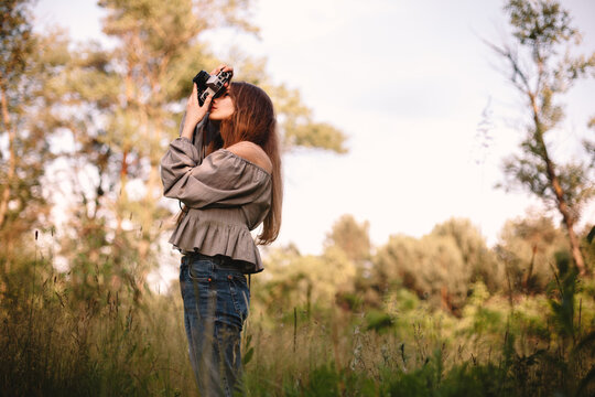 Young woman photographing with camera while standing in summer forest