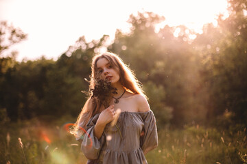 Young woman holding bouquet of dried flowers standing on summer field