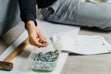 Close up on midsection of unknown caucasian man holding electric screwdriver while putting together Self assembly furniture of plywood screwing screws following instructions - DIY concept copy space