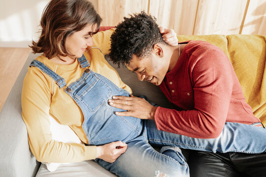 Black man touching belly of pregnant woman at home.