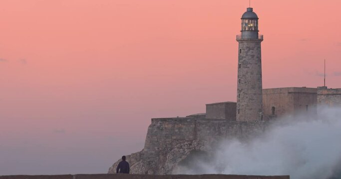 wave crashing on malecon with the Faro Castillo del Morro lighthouse. Havana, Cuba