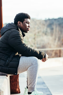 Portrait of an African American boy sitting on a bench in an urban space.