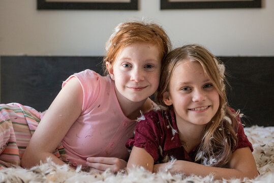 Two happy young girls having a feather pillow fight on the bed.