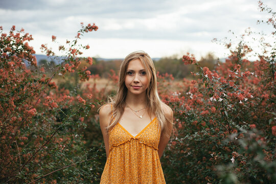 A young woman in a dress stands among flowering shrubs with the Blue Ridge Mountains in the background