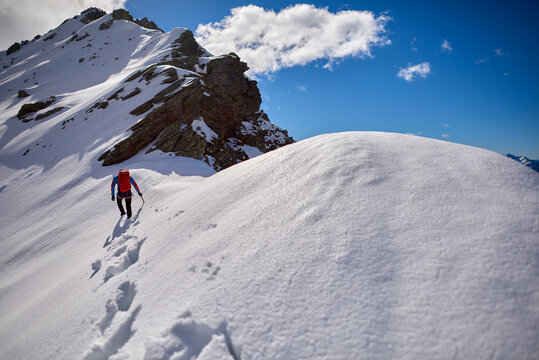 Man climbing a snowy mountain on a sunny day in Devero, Italy.