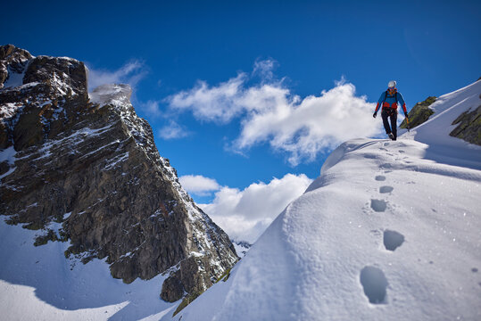 Man climbing a snowy mountain on a sunny day in Devero, Italy.