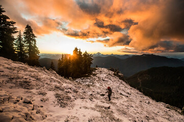Backpacker hikes over snow on rocky mountain ridge.