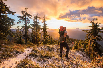 Front view of backpacker hiking over scenic mountain ridge at sunset