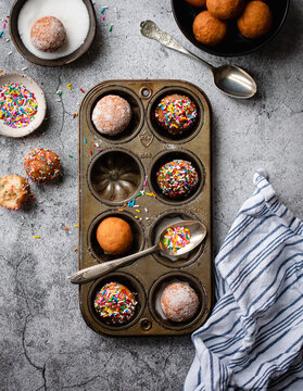 Overhead of donut holes covered in sugar and sprinkles in baking tin.