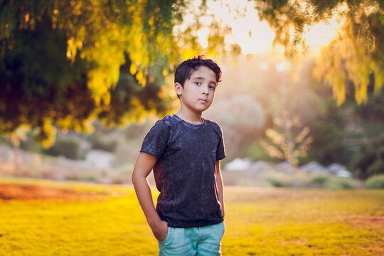 Boy standing in front of back lit pepper trees in the afternoon.