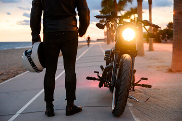 Young man standing near motorbike and enjoying sunset view