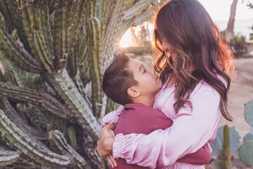 Mother hugging son, both looking at each other with back light sun.