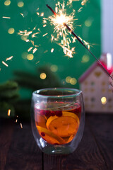 christmas cocktail on a wooden table with a green background and lights and a glowing house with a sparkler