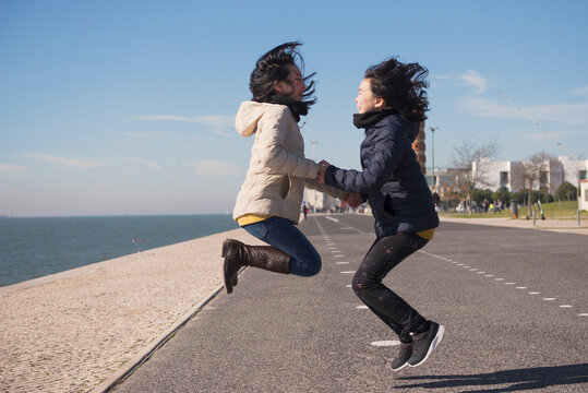 Joyful girls are jumping on the banks of the river in the city.