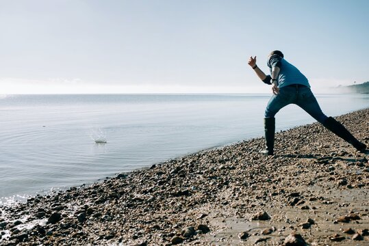 man skimming a stone in the ocean on a sunny day in the UK