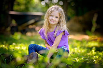 Beautiful little blond girl in purple shirt sitting on the grass.