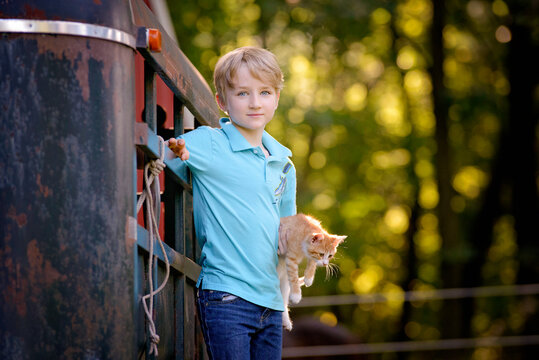 Handsome blond boy holding a kitten outdoors in rural setting.