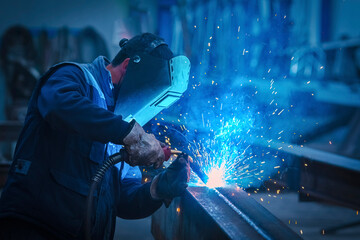 Man with protective face and eye shield welding industrial steel beam