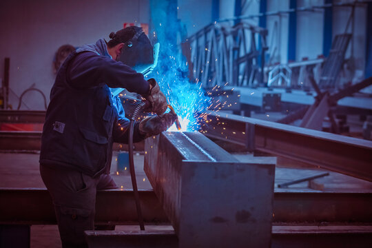 Man with protective face and eye shield welding industrial steel beam