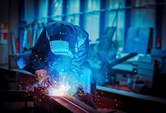 Man with protective face and eye shield welding industrial steel beam - Powered by Adobe