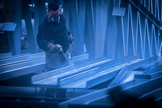 Man with protective mask painting and lacquering steel with compressor