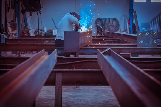 Man with protective face and eye shield welding industrial steel beam