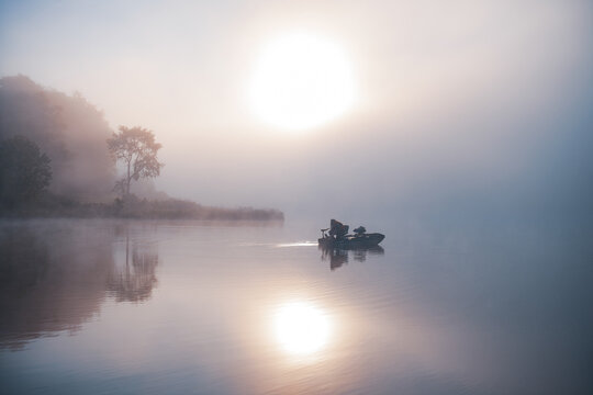 Silhouetted Boaters on Idyllic Lake during Colorful Foggy Sunrise