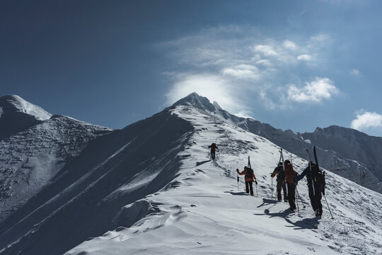 Rear view of people with backpacks and splitboards climbing snowcapped mountain against sky