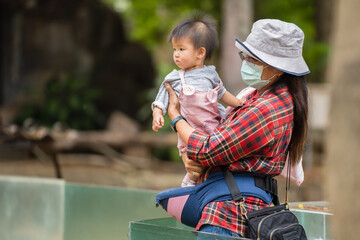 woman with medical mask to protect coronavirus(covid-19) while holding baby in zoo