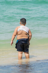A plump Asian boy walks into the sea for a swim.