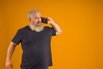 a man with a gray beard and hair in a black t-shirt talking on the phone, yellow background