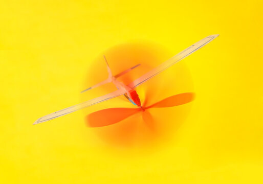 Balsa wood rubber band powered toy airplane with propeller on a yellow background