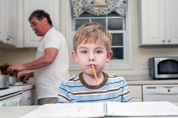 Young boy being silly with pencil in his mouth, distracted while doing homework