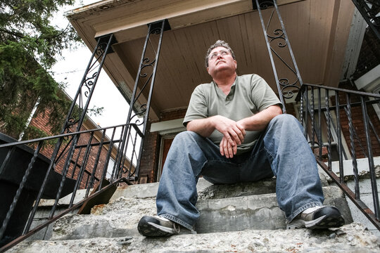 Middle aged man sitting on the steps of a house in the inner city