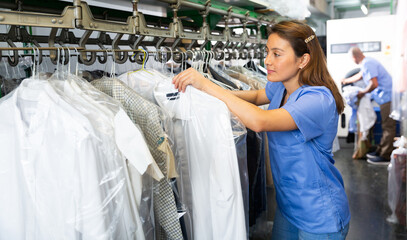 Adult female worker of laundry inspecting clothing after dry cleaning on racks