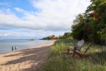Adirondack chairs on the shore of Lake Superior in Marquette, Michigan. Harbor Lighthouse in the...