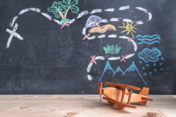 Wooden toy airplane on the background of a chalk board with a drawing of the travel route. The concept of vacation plans