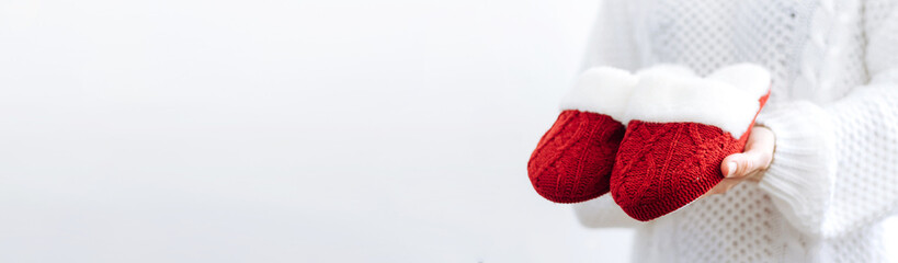 Woman in white sweater holds warm knitted red slippers. Concept of home family cozy holiday Christmas New Year.