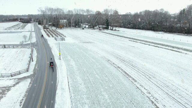 Aerial of Amish horse and buggy on road in Lancaster County Pennsylvania during winter snowstorm.