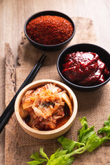 Korean kimchi cabbage with gochujang (red chili paste) and chili powder in bowl on wooden background