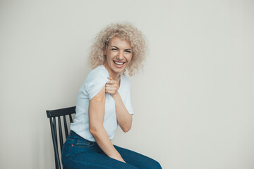 Happy caucasian woman showing vaccinated arm with adhesive bandage. Curly hair. Adult immunization,...