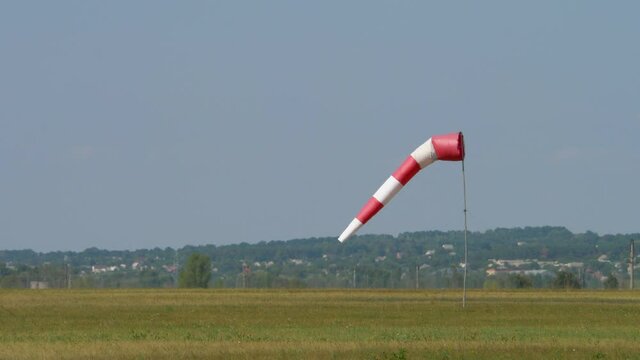 Striped cone airsock indicator of wind direction and speed. Red white windsock swings in wind on sky background. Visual signal at airport