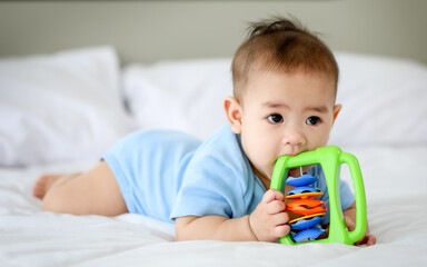 Adorable and innocent little Asian baby enjoys playing fun with colorful children toy while lying...