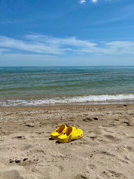 Bright yellow crocs footwear on the beach, copy space for text. Yellow trendy croc beach shoes. Vacation concept.